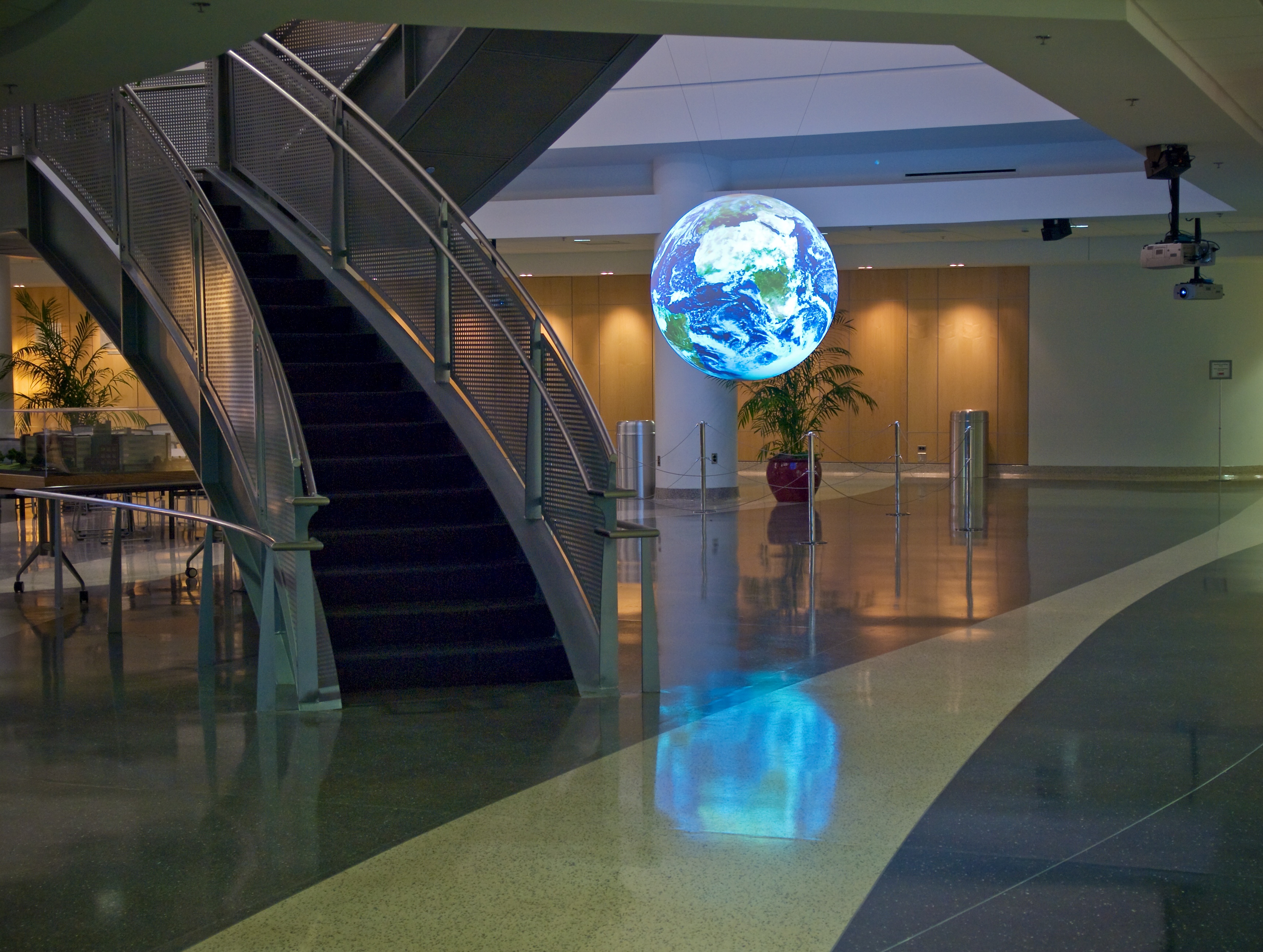 Science On a Sphere displays satellite imagery of Earth in a well-lit lobby. In the foreground is a staircase leading up to a balcony above the Sphere