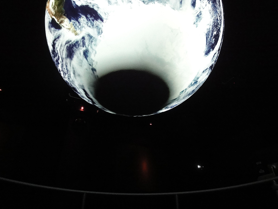 A dark circle is visible at the bottom of Science On a Sphere while it displays satellite imagery of Earth