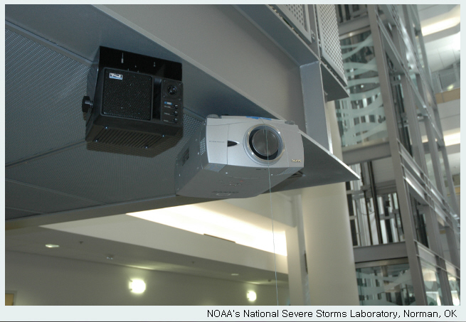 A projector is mounted close to the ceiling next to a speaker