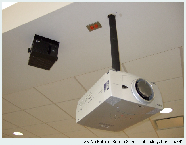 A projector is mounted to a pole that extends through a hole cut in the ceiling