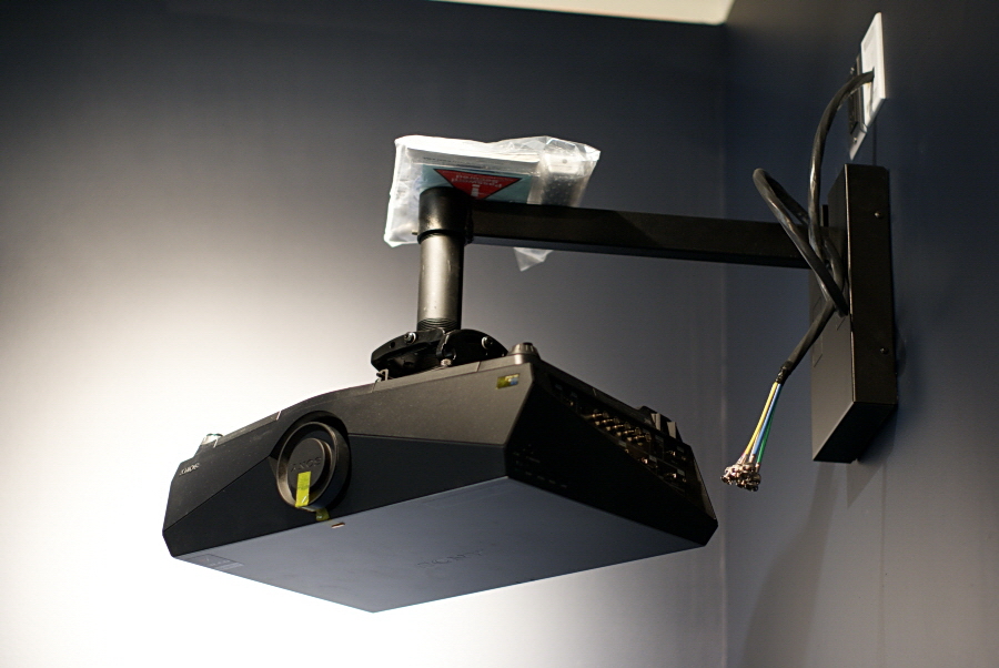 A projector is mounted to the wall by a short arm that extends out and down