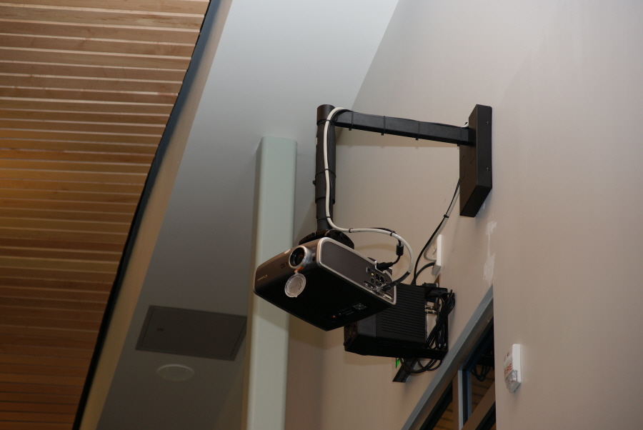 A projector is mounted to the wall by an arm that extends out from the wall and then down