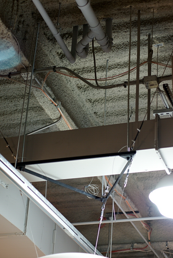 A black metal frame in the shape of an equilateral triangle is dropped down from the ceiling by solid metal rods around some duct work. Science On a Sphere is attached by wires to the corners of the triangle