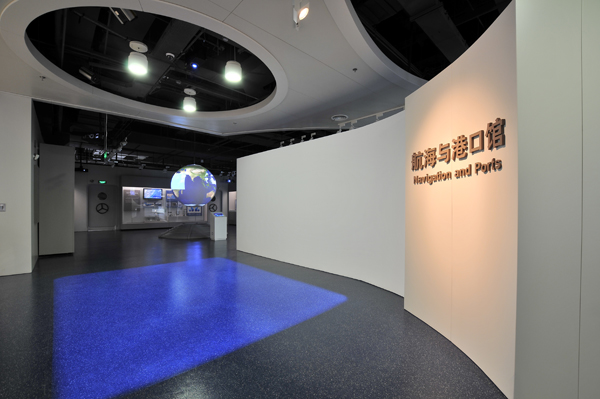 Science On a Sphere is visible in the distance of a large exhibit space. A sign reading 'Navigation and Ports' in Mandarin and English is visible in the foreground, along with a large blue square projected onto the floor