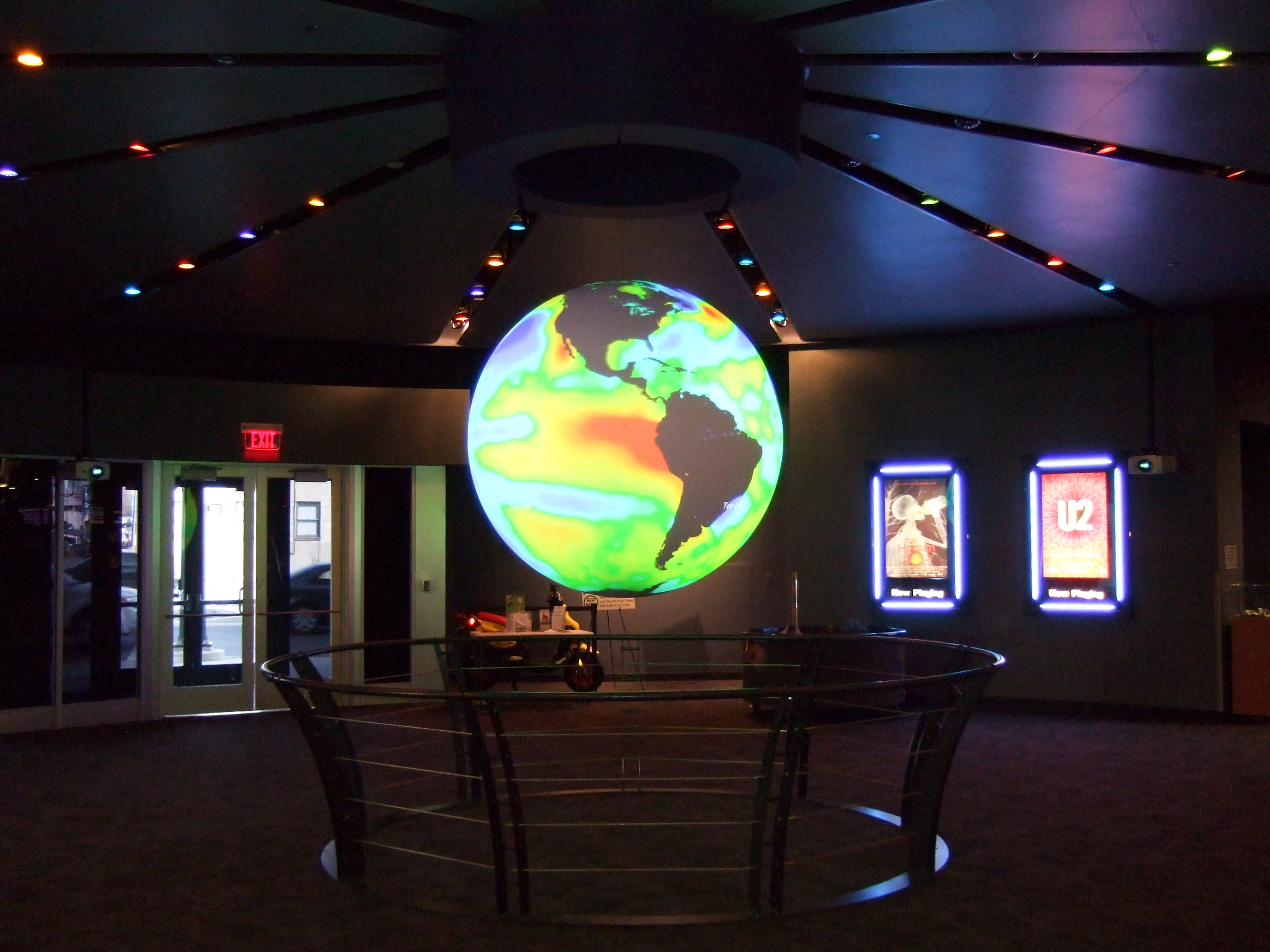 Science On a Sphere hangs in the center of a lobby displaying ocean data in hues of red, yellow, green, and blue