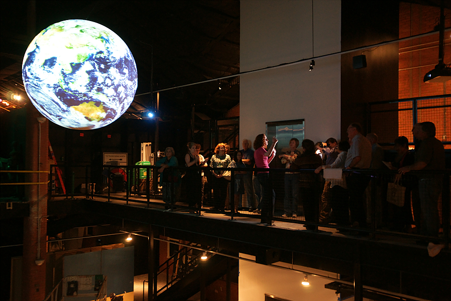 A group of people stand on a balcony watching a presentation on Science On a Sphere