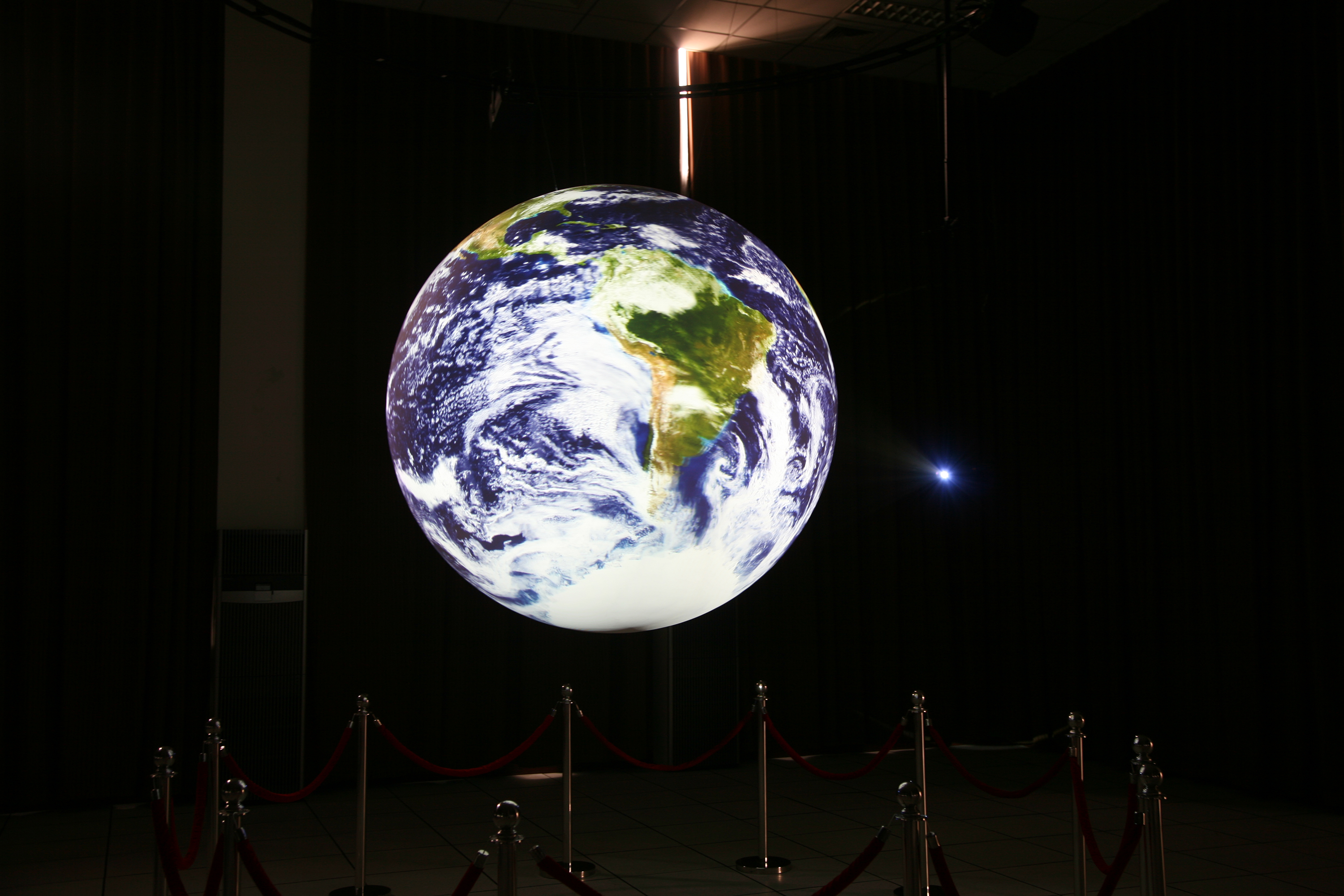 Science On a Sphere displays satellite imagery of Earth in an empty room, cordoned off from visitors by a red velvet rope