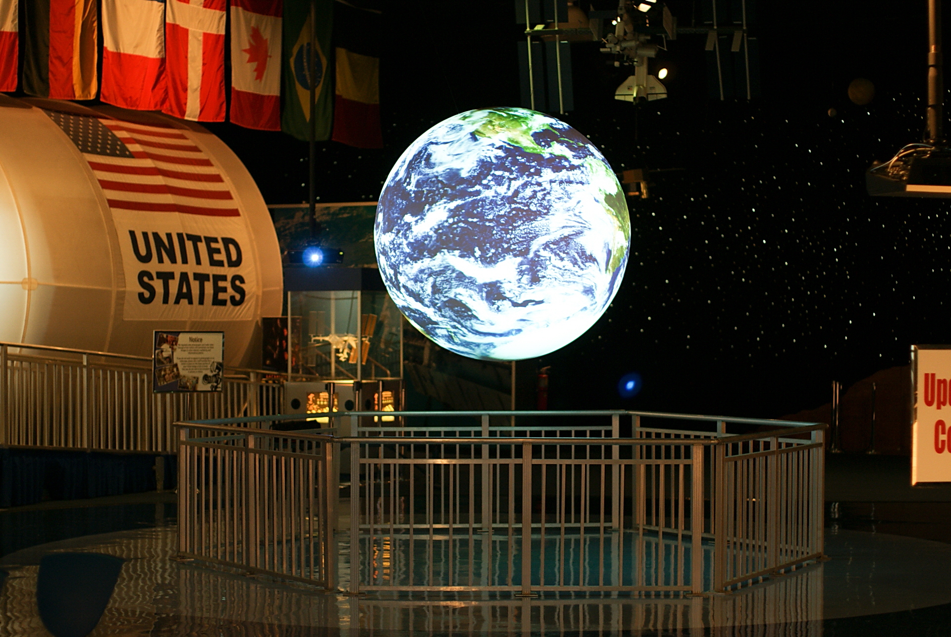 Science On a Sphere hangs in an empty exhibit space. Other exhibits related to space exploration are visible int he background