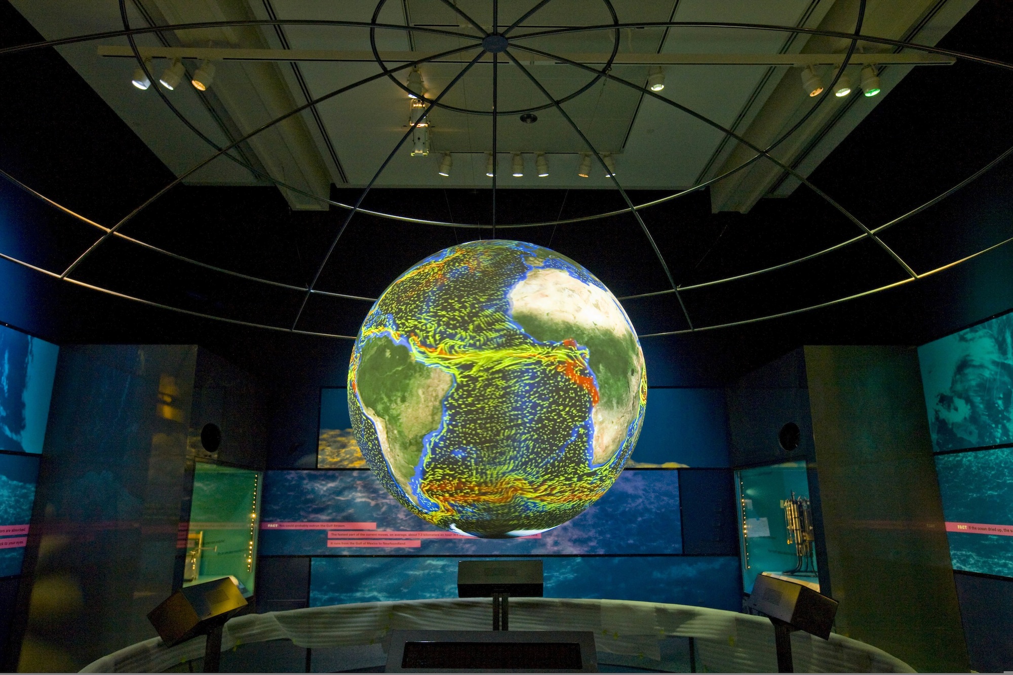 Science On a Sphere displays ocean currents as lines of red, yellow, green, and blue in an empty room. Behind it, some glass display cases are visible