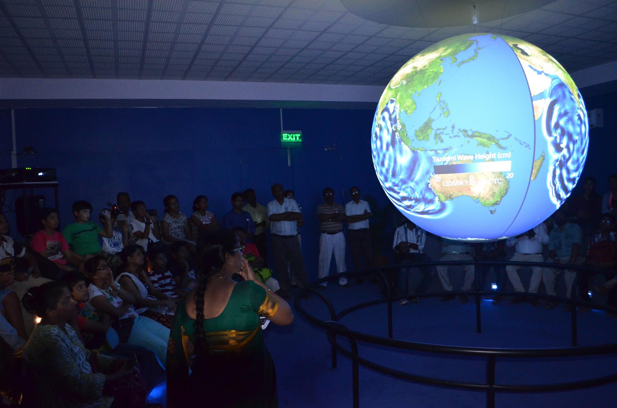 A group of people watch Science On a Sphere as it displays data from a tsunami in the Indian Ocean. The Sphere's display is split so that the two hemispheres of the Sphere show the same data, rather than a complete image of the Earth
