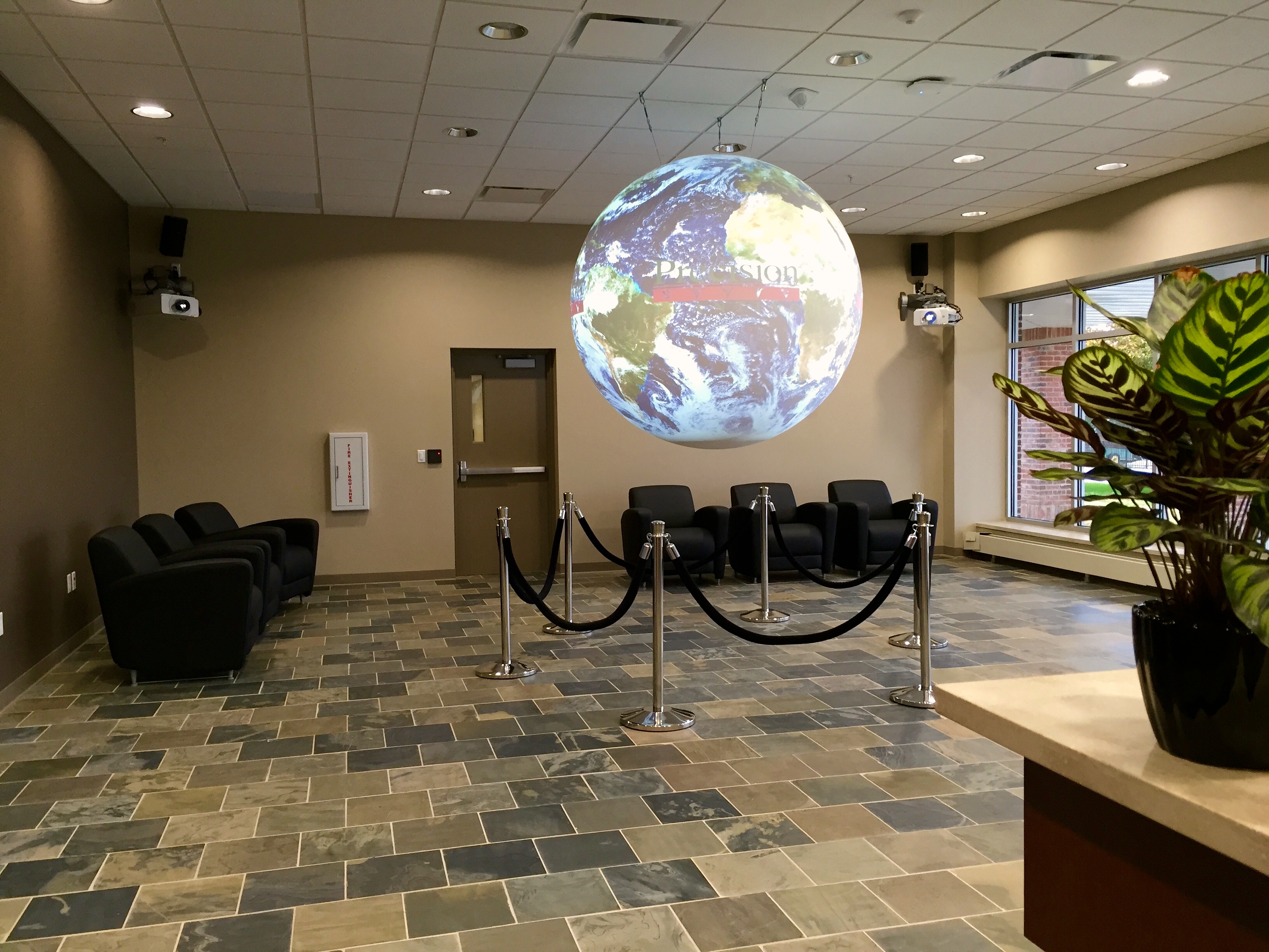 Science On a Sphere hangs in a well-lit lobby displaying the Precision Planting logo over a satellite image of the Earth