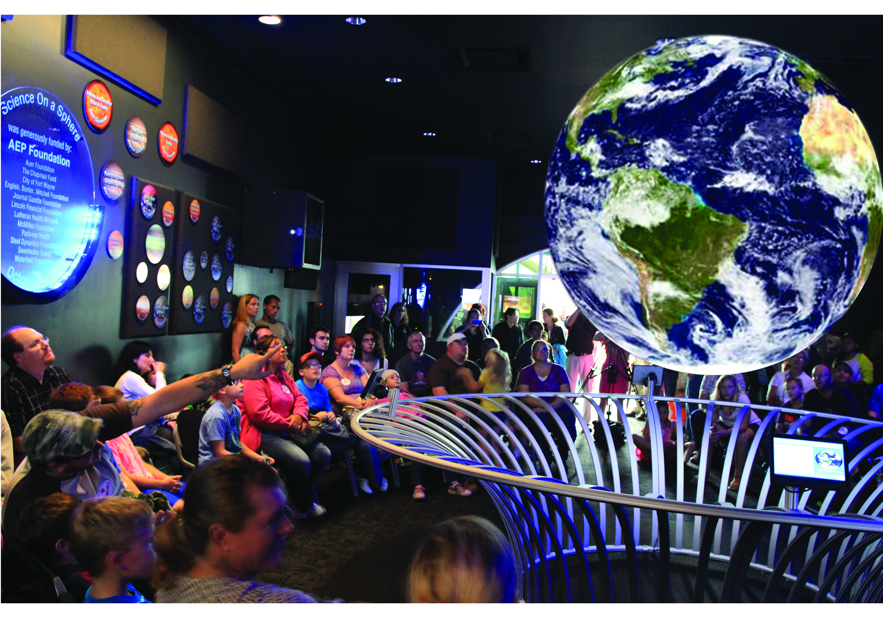 A large crowd of people surround Science On a Sphere looking at satellite imagery of Earth