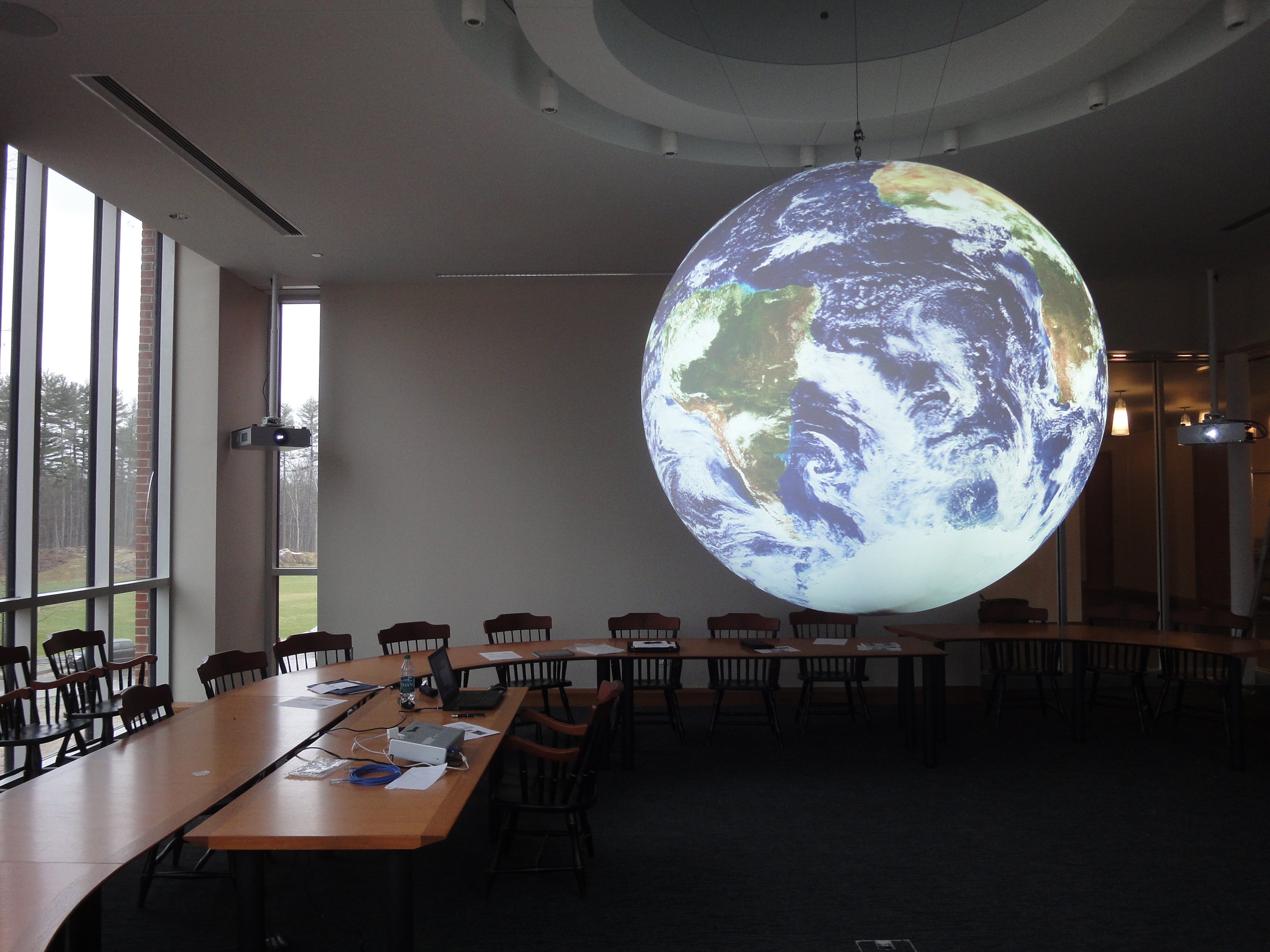 Science On a Sphere hangs in an empty room surrounded by a long, curved conference table with wooden chairs