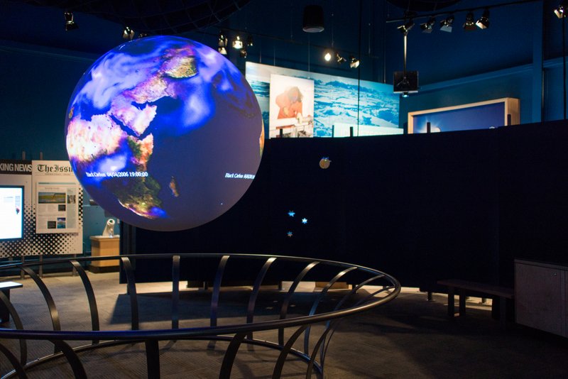 Science On a Sphere displays atmospheric data in an empty exhibit space. Other exhibits are visible in the background