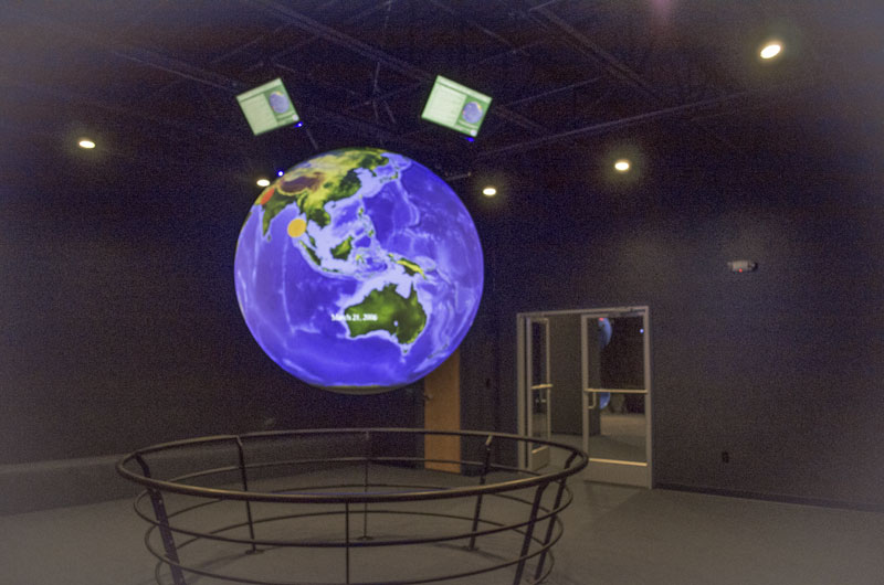 Science On a Sphere hangs in an empty theater with four monitors mounted above it