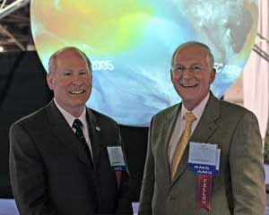 Two men in suits smile for the camera. In the background, Science On a Sphere displays a colorful dataset