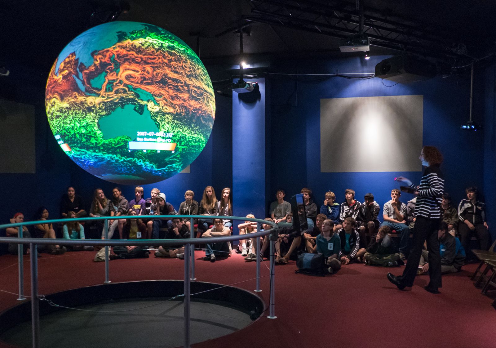 Students sit on the floor around Science On a Sphere watching a presentation