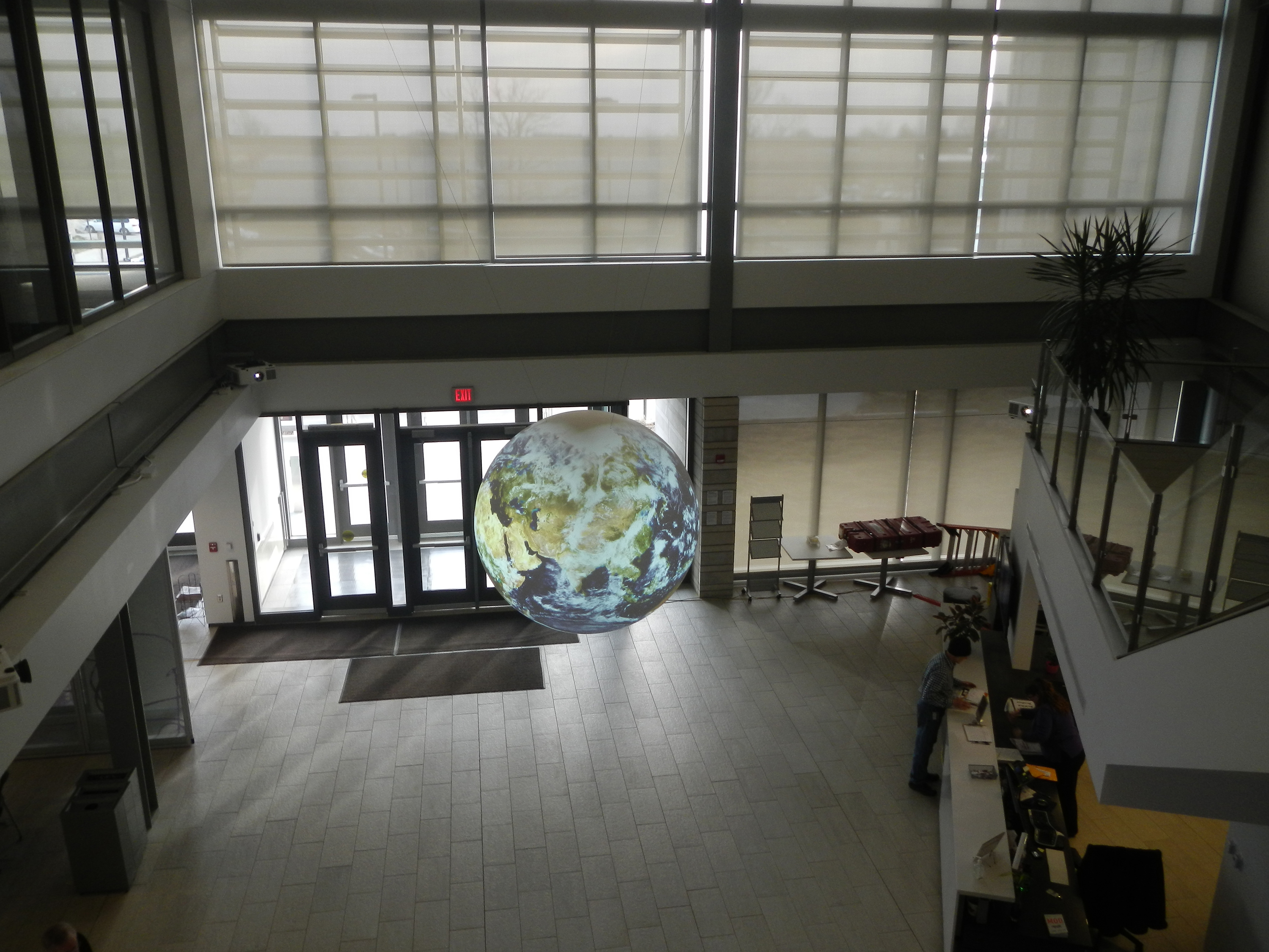 The camera looks down from a second floor balcony to Science On a Sphere hanging in a lobby