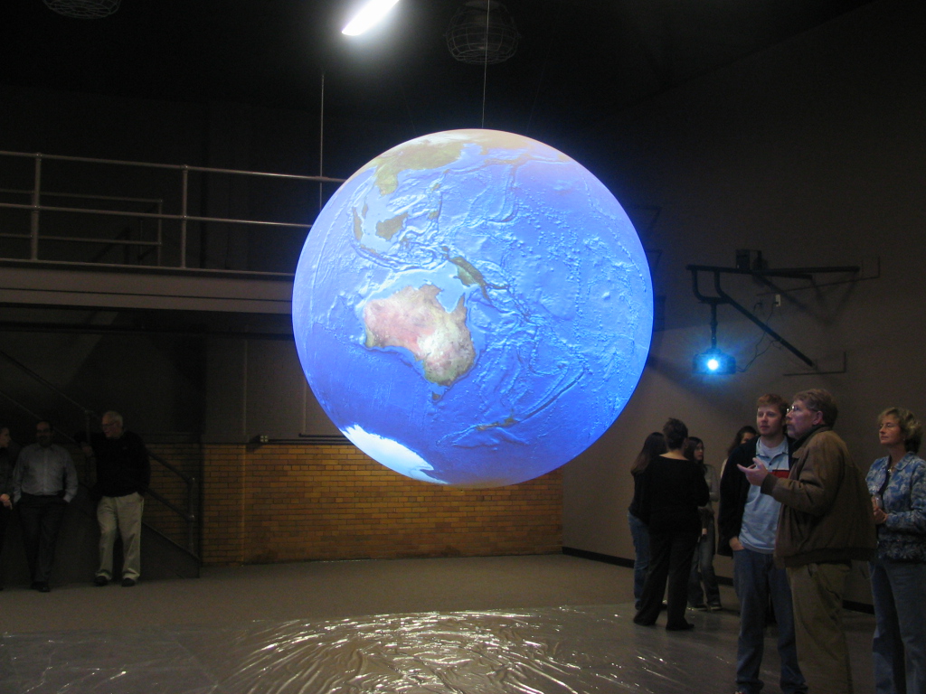 Science On a Sphere displays bathymetric data as a few people stand and watch 